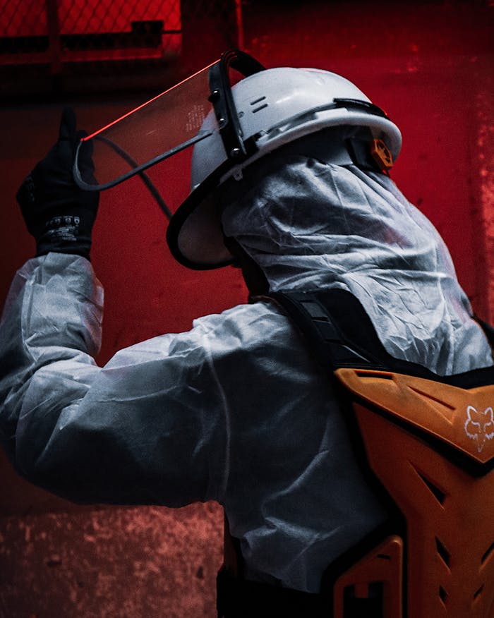 Worker in protective clothing and helmet at a construction site lit in red tones.