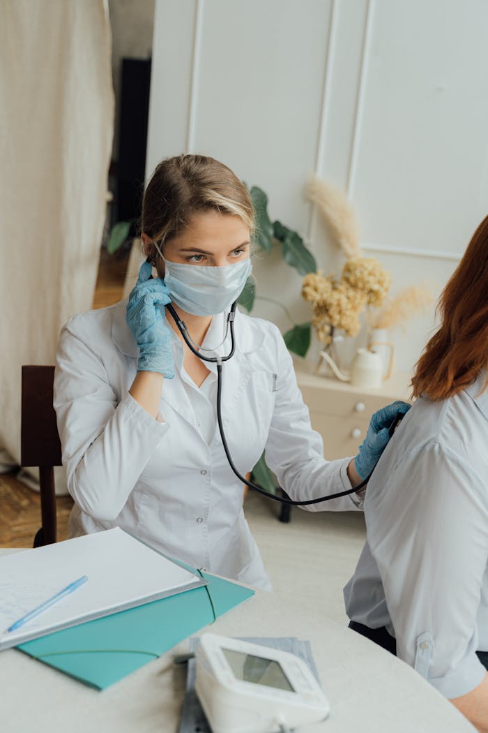 A healthcare professional in PPE using a stethoscope for a medical check-up.